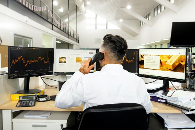 a man on the phone in front of his desk looking at the monitors with statistics displayed 