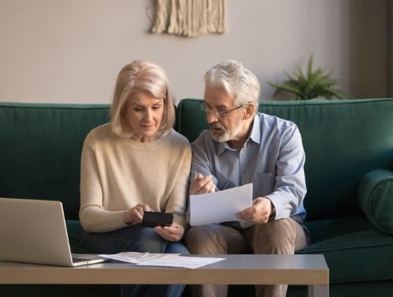 an elderly couple in their living room looking at paperwork and a phone